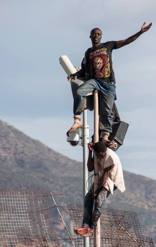 African migrants sit on top of a border fence between Morocco and Melilla